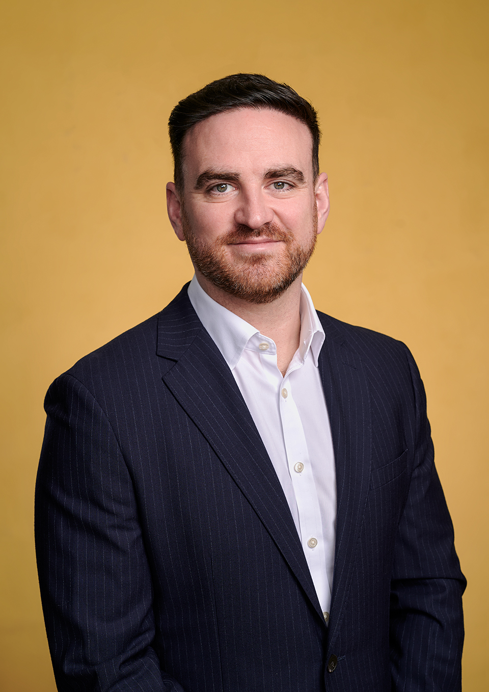 Relaxed business portrait of Eunan in a suit without a tie, London studio with a yellow backdrop