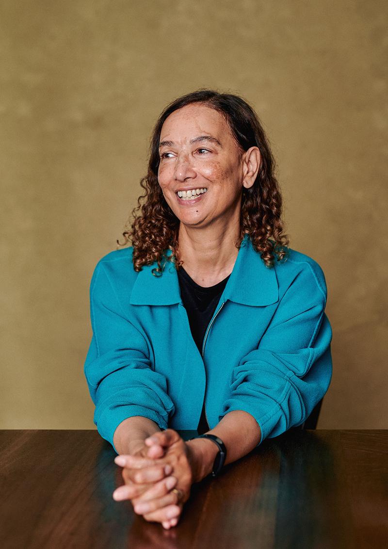 Portrait of author Jacqueline Crooks in-studio with a table and painted canvas backdrop.