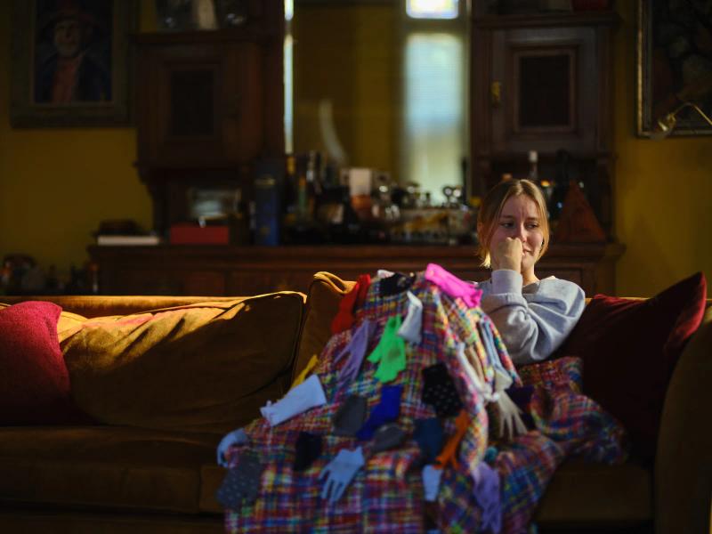 Actress in character holding a patchwork quilt on a sofa during filming of a short film