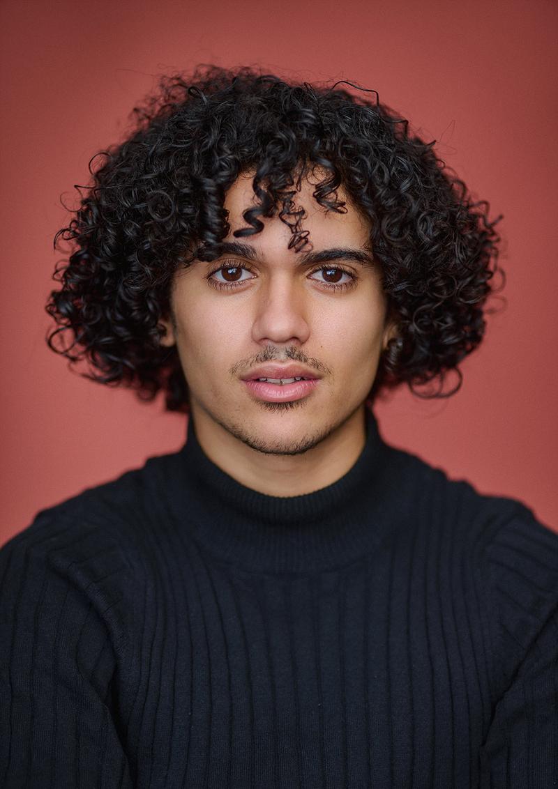 Daylight actor headshot with a terracotta backdrop.