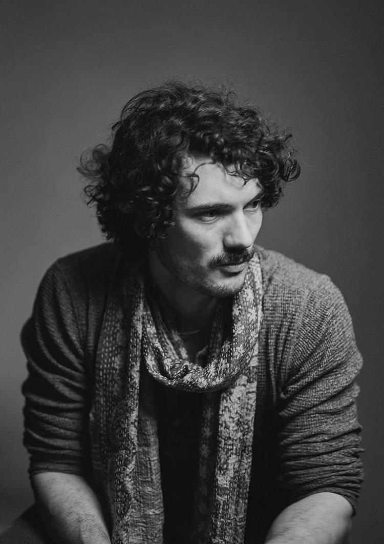 Black and white seated studio portrait of actor Rowland Sterling with contrasting shadows and a gradient backdrop.