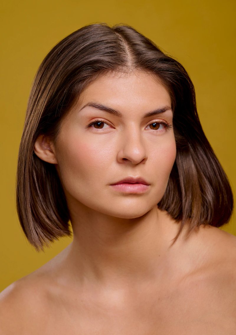 Beauty portrait of model Natalie with a sleek brown bob, bare shoulders and natural makeup, against a mustard yellow backdrop in my London studio.