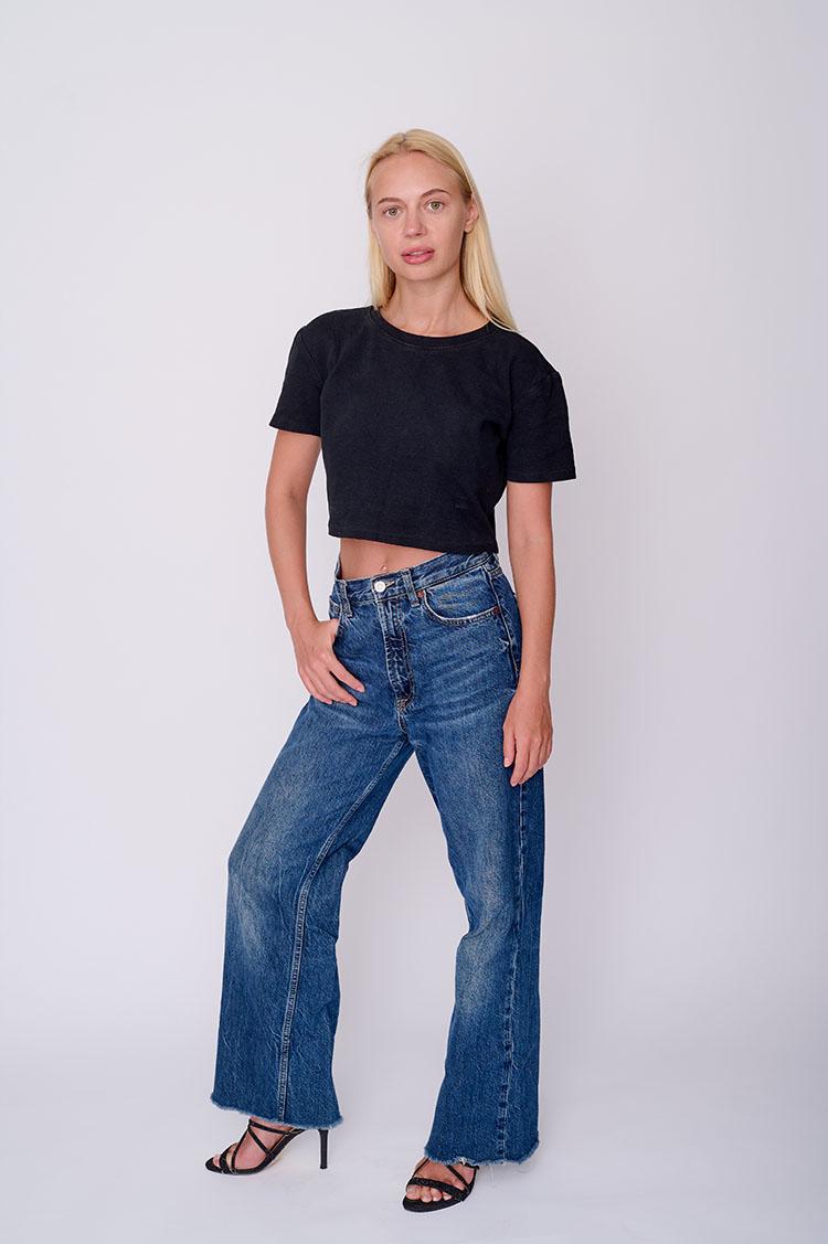 Digital of model Anastasia in-studio wearing jeans and black t-shirt with full length white backdrop.