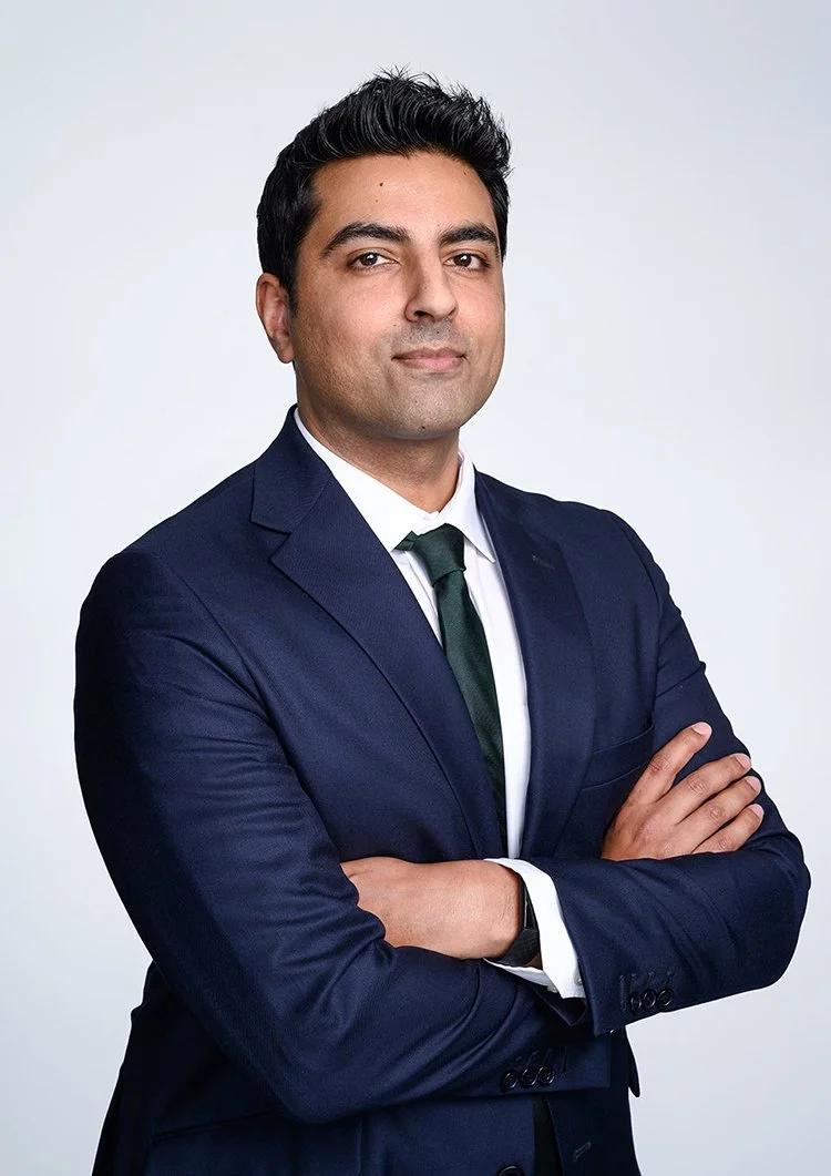 Corporate headshot of a businessman in a navy suit with folded arms, photographed on location at a London office.
