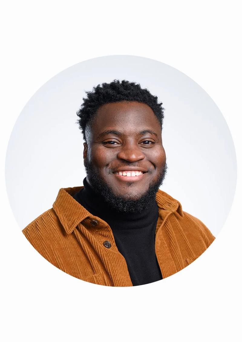 LinkedIn headshot of Tariq smiling in a tan corduroy jacket, photographed against a plain white background in London.