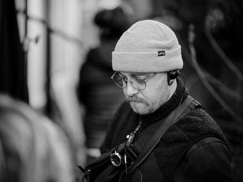 Black and white behind the scenes photograph of an assistant director in a beanie and headset on a London film set.