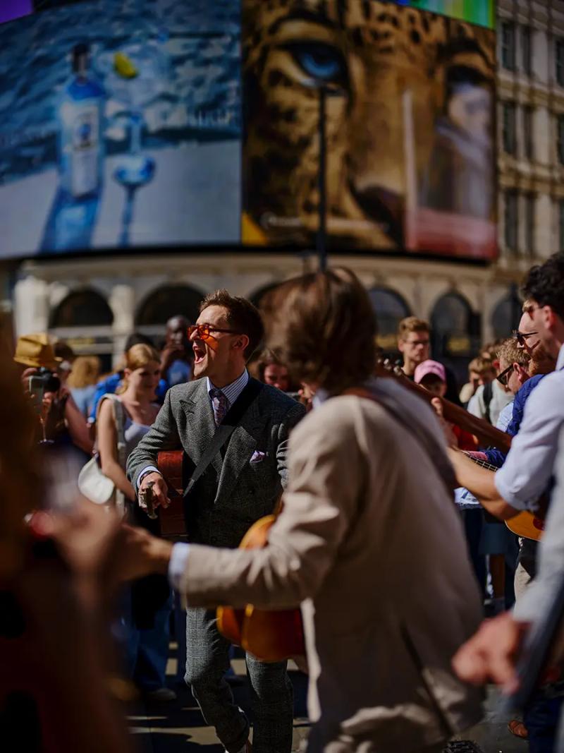 Documentary photograph of the band The London Essentials performing to a crowd under the screens at Piccadilly Circus in London.